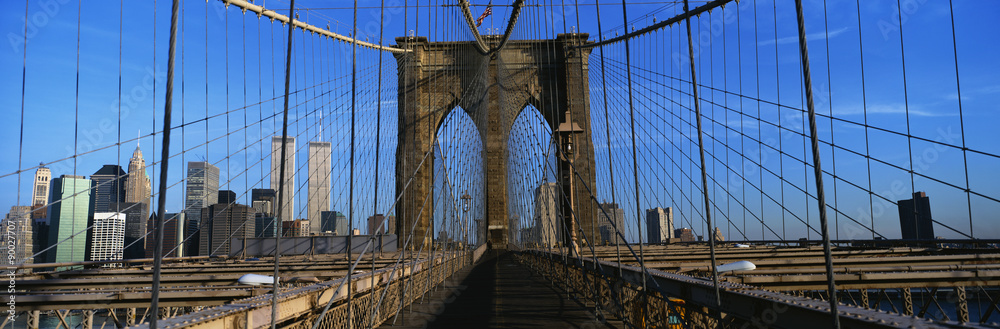 Fototapeta premium This is a close-up of the Brooklyn Bridge Walkway to Manhattan. The Manhattan skyline is in the background. The steel fencing is on either side of the bridge.