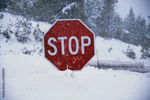This is a stop sign after a freshly fallen snow. The snow is piled up high underneath the stop sign. The background indicates a snowy landscape. © spiritofamerica