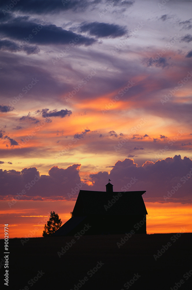 This is a silhouette of a farm at sunset. There is a pinkish, orange glow in the sky.