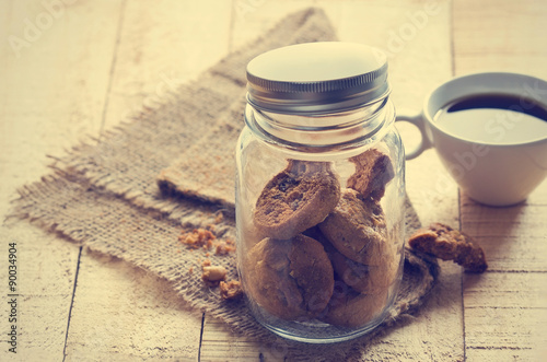 Chocolate chip cookies in glass jar on sack and coffee on wooden