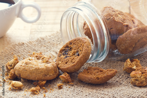 Foto Chocolate chip cookies in glass jar on sack and coffee on wooden