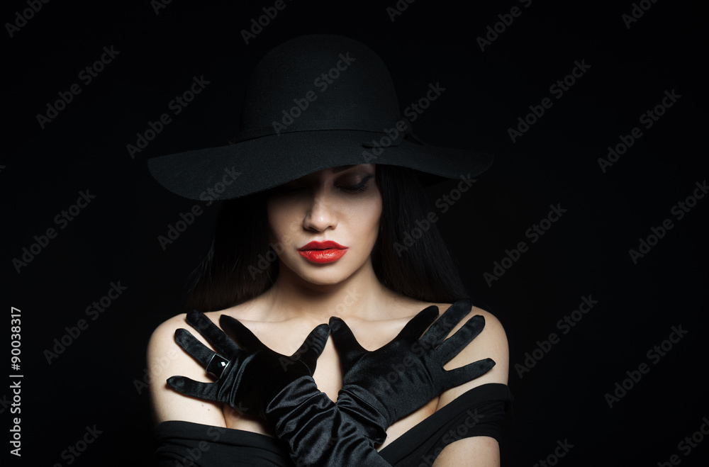Woman in big black hat with arms across, studio portrait, dark background Woman in big black hat with arms across, studio portrait, dark background