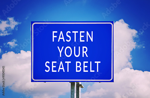 Fasten Your Seat Belt text on blue road sign with sky background