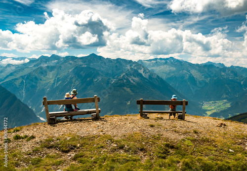 family relaxing on benches in autumn austrian mountains with peaks view