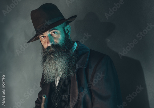 Spooky vintage beard man with rifle in 1900 style fashion agains