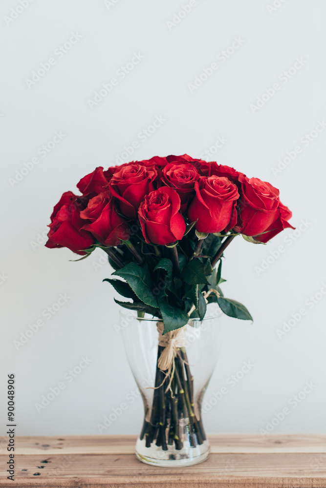 Bouquets of roses in three glass vases next to a watering can on a white wall Bouquets of roses in three glass vases next to a watering can on a white wall