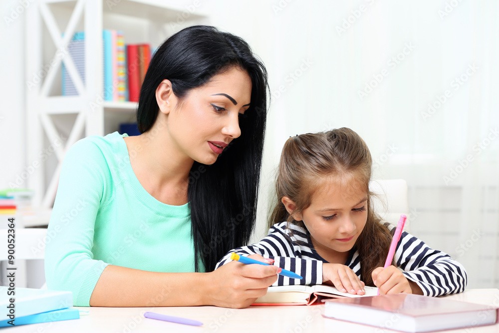 Beautiful school girl doing homework with mother at home