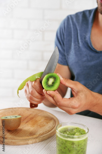 Young man peeling kiwi, preparing orange juice