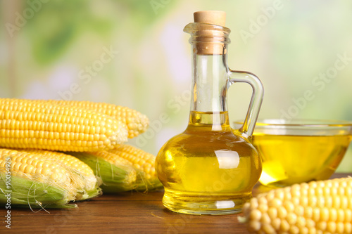 Fresh corn with bottle of oil on bright background