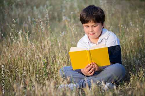 little boy reading book in the meadow