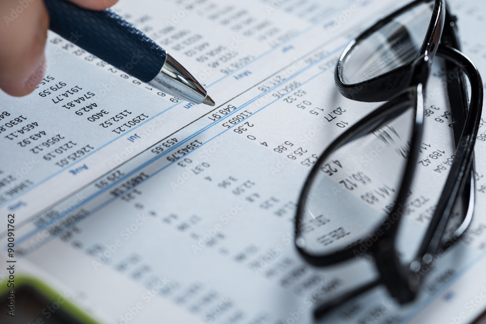 Person Hand With Pen And Glasses Over Financial Paper Person Hand With Pen And Glasses Over Financial Paper