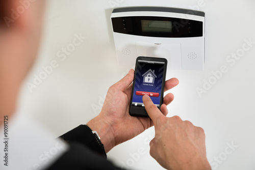 Businessperson Disarming Security System With Mobile Phone