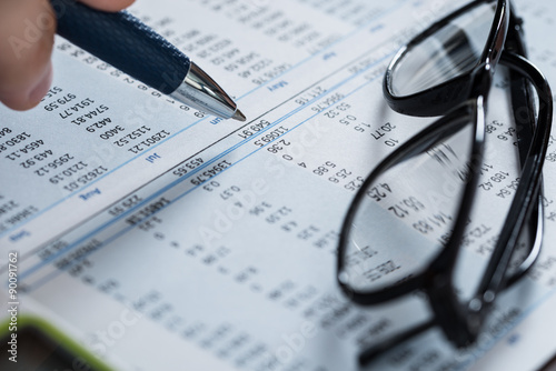 Person Hand With Pen And Glasses Over Financial Paper