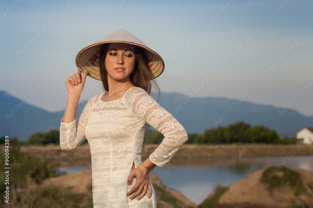 blonde girl in Vietnamese dress smiles against country lakes