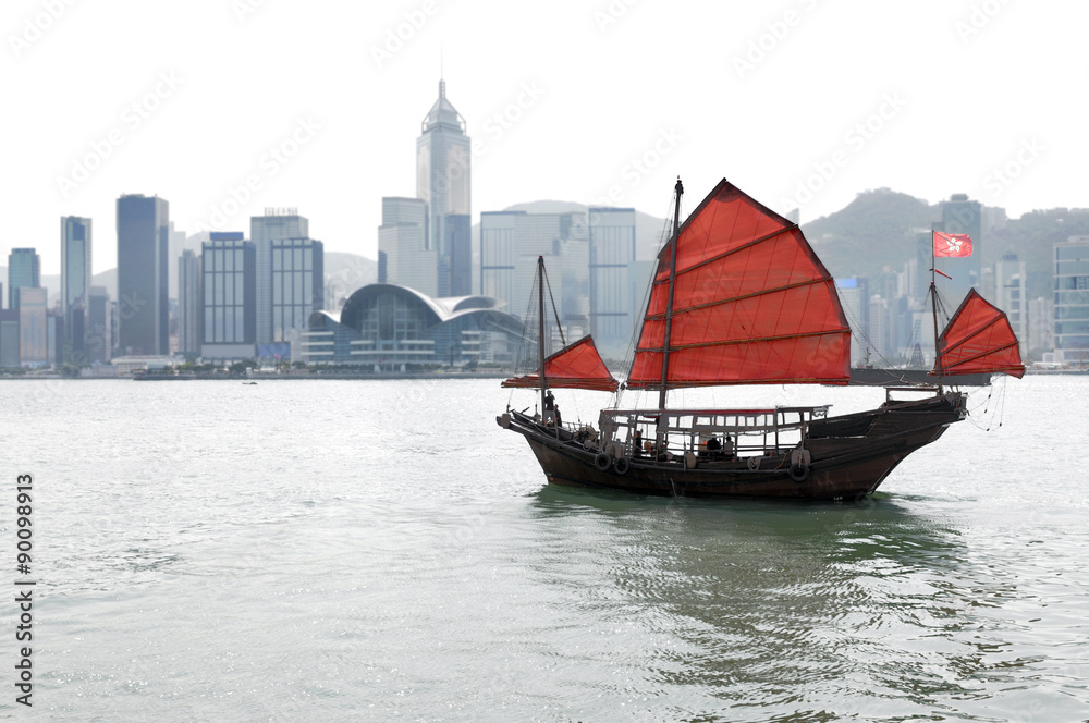 Naklejka premium Hong Kong city skyline with traditional junk sailing boat and red sails