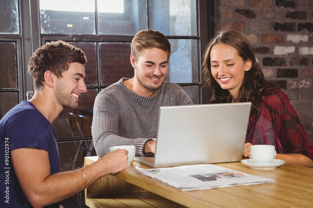 Smiling friends having coffee together and looking at laptop Smiling friends having coffee together and looking at laptop
