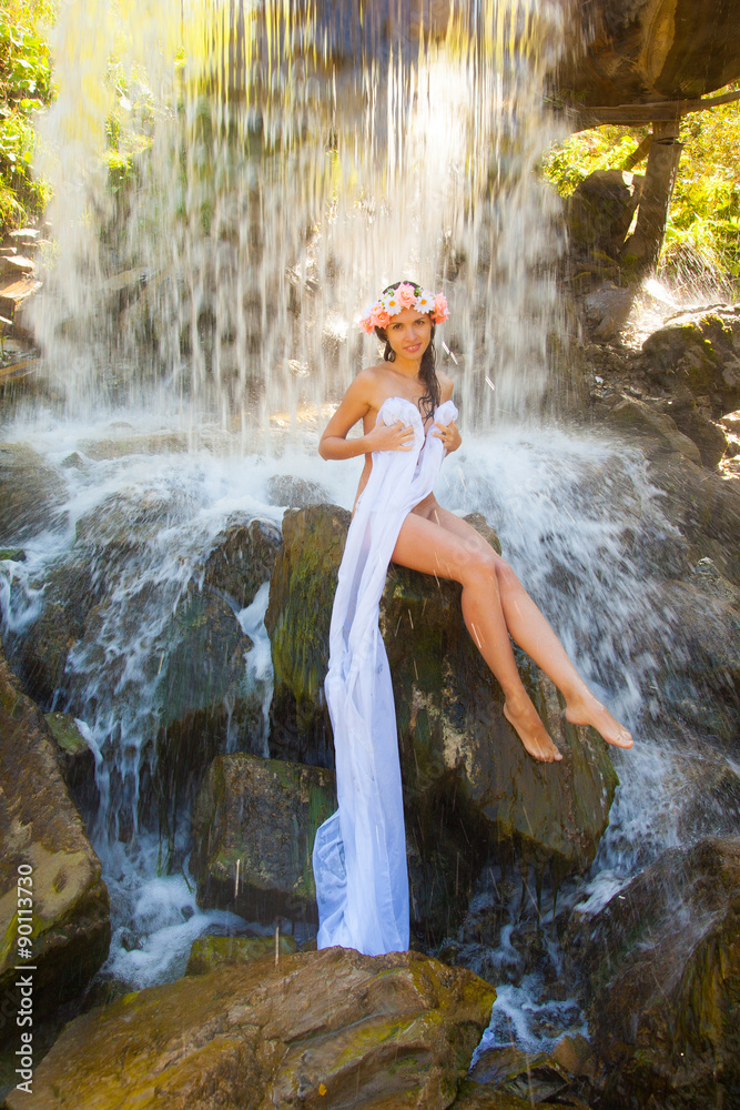 Naked girl in a wreath at the waterfall.
