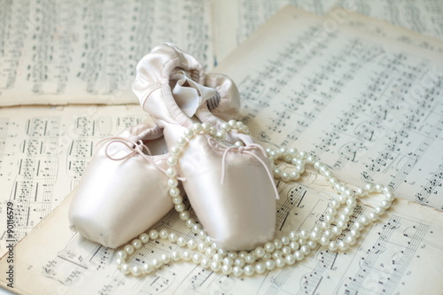 Ballet shoes and necklace laying on the old piano musical notes