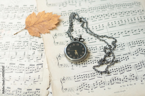 Old watch and dead tree leaves laying on old piano musical notes