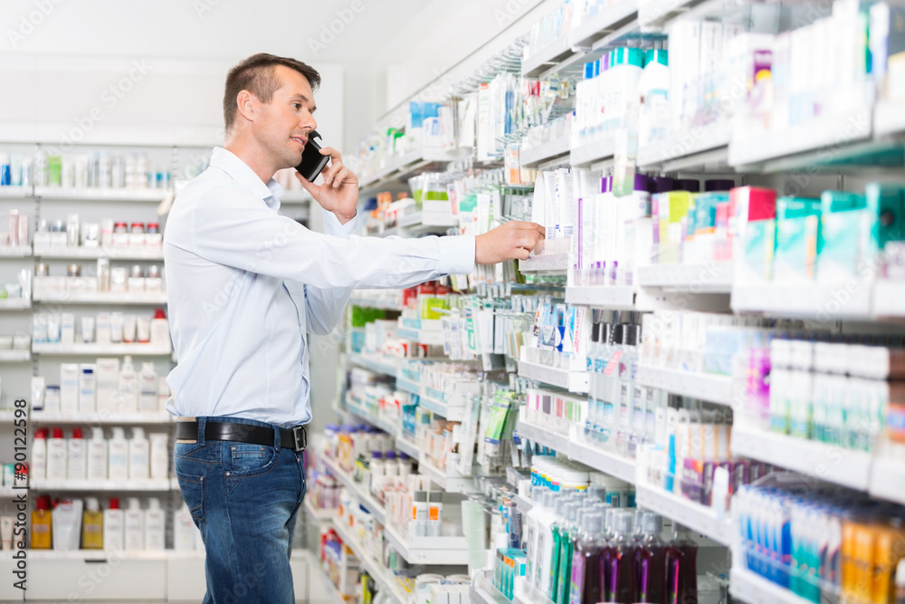 Man Using Mobile Phone While Selecting Product In Pharmacy