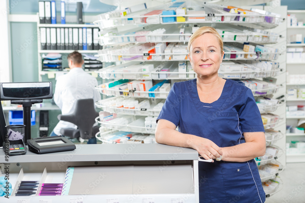 Smiling Pharmacist Leaning At Cash Counter In Pharmacy