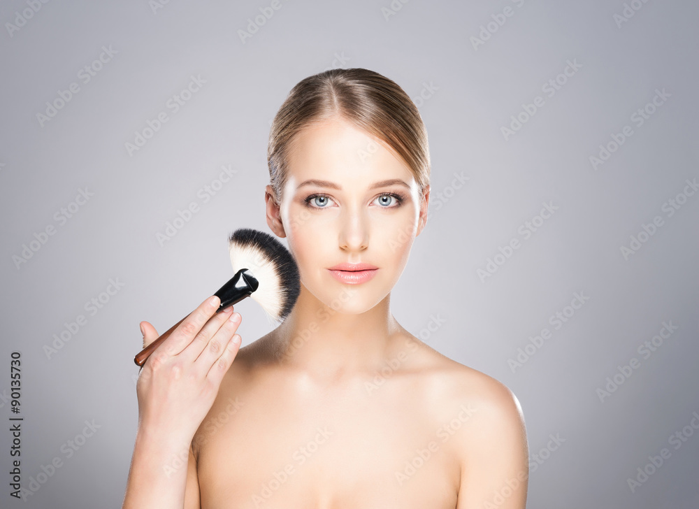 Attractive young woman applying powder on her cheeks. Attractive young woman applying powder on her cheeks.