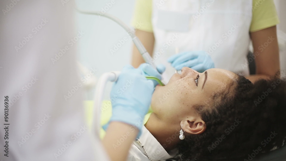 Young african american woman patient in the dental clinic on treatment. Hands of dentist and assistant during visit of customer Young african american woman patient in the dental clinic on treatment. Hands of dentist and assistant during visit of customer