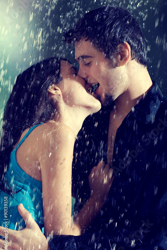 Young couple hugging and kissing under a rain, in passion