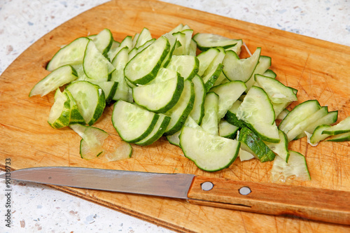 Fresh sliced cucumber and knife on wooden cutting board.