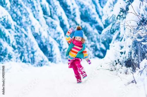 Little girl playing in snowy winter forest