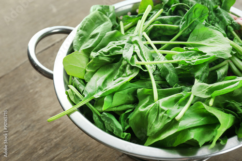 Fresh spinach leaves in colander on wooden table, closeup