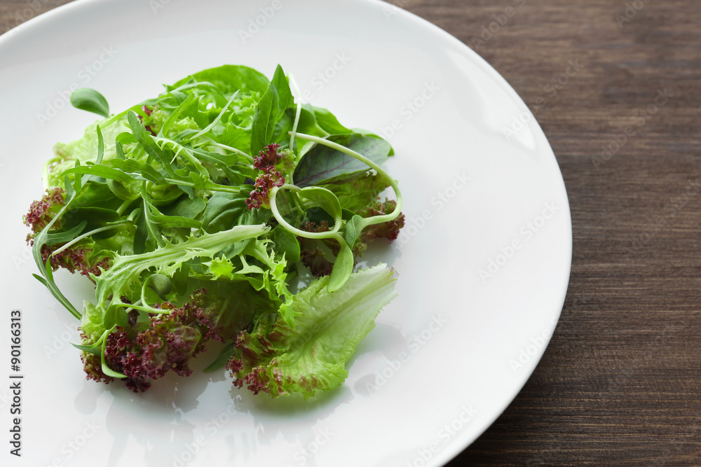 Plate of fresh mixed green salad on wooden table close up Plate of fresh mixed green salad on wooden table close up