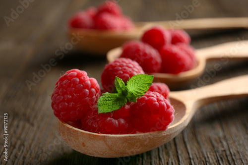 Fresh red raspberries in spoons on wooden table, closeup