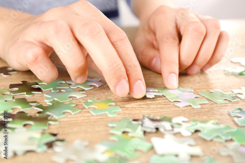 Female hands assembling puzzle on wooden table, closeup