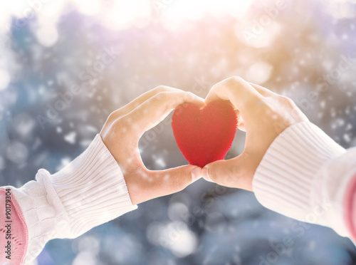 Female hand holding red heart up to the sun during morning with a snow in winter   love and valentine concept