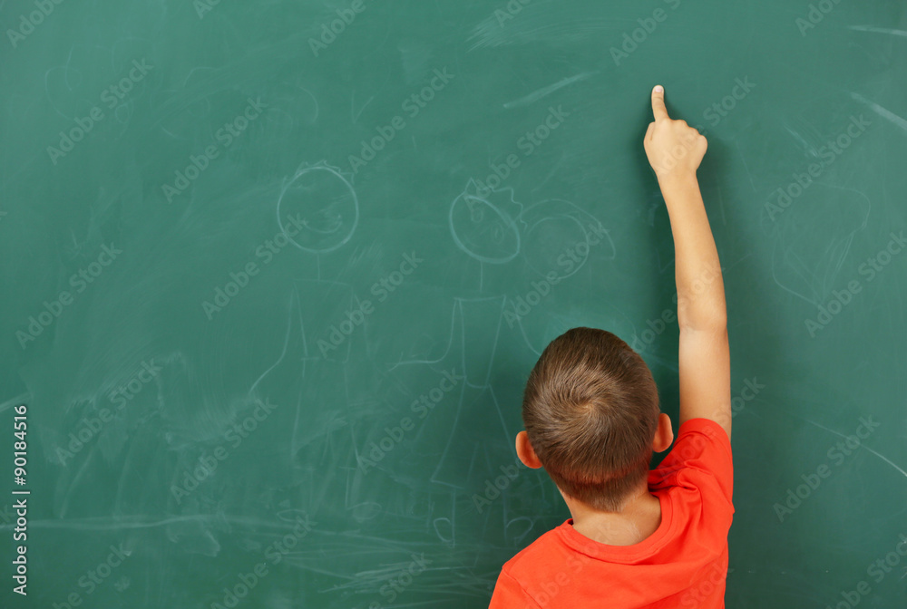 Little boy pointing at something at black chalkboard in classroom Little boy pointing at something at black chalkboard in classroom