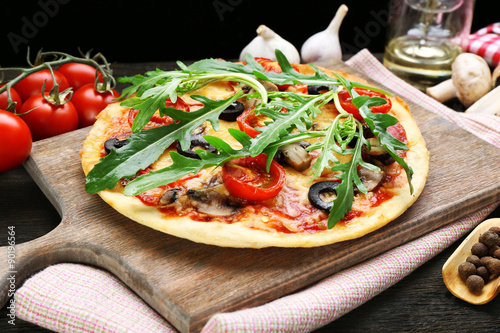 Tasty pizza with vegetables and arugula on cutting board on table close up