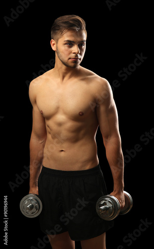 Muscle young man holding dumbbells on dark background