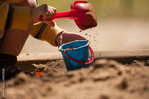 In the sandbox. / Pour sand into the bucket in the sandbox.