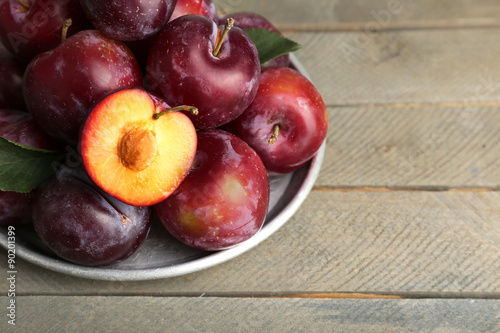 Ripe plums in metal plate on wooden background