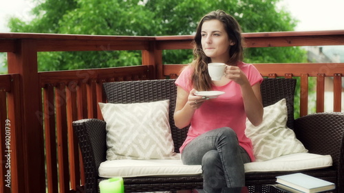 Girl drinking coffee and smiling to the camera on the terrace
