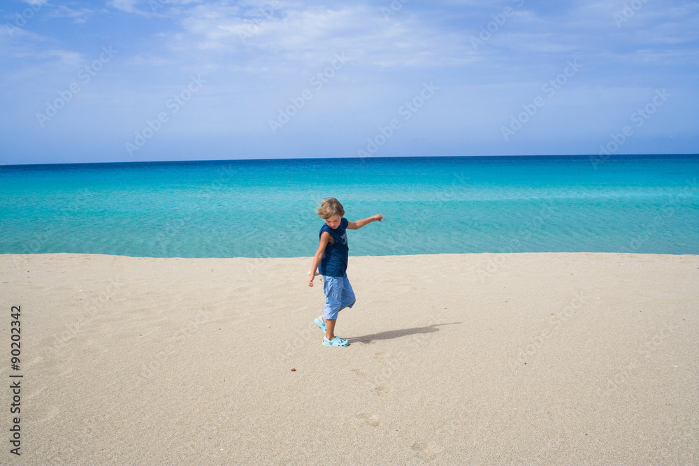 Little boy playing and dancing in the ocean on a tropical beach