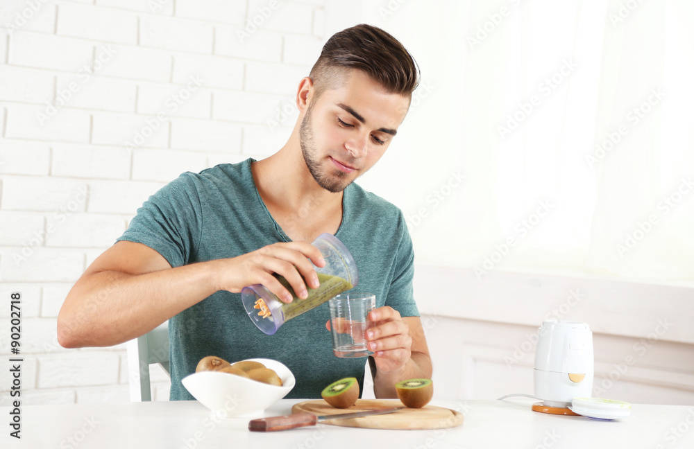 Young man man pouring fresh kiwi juice into glass