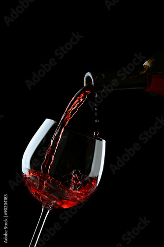 Red wine pouring into wine glass on black background