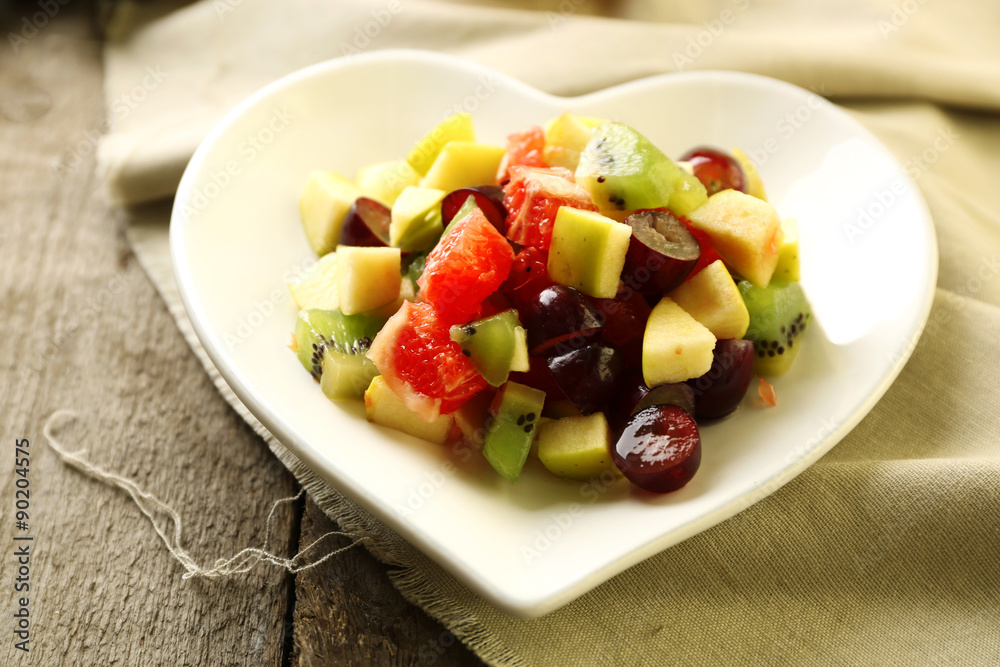 Fruit salad on plate, on wooden background