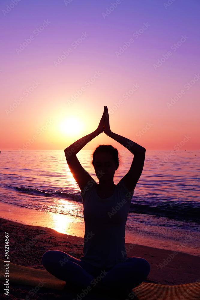 Young healthy woman practicing yoga on the beach at sunset