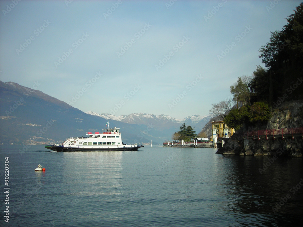 Tranquil lake landscape on Lake Como in Lombardy, Italy, on a quiet sunny morning, with snow covered mountain tops in the distance.
