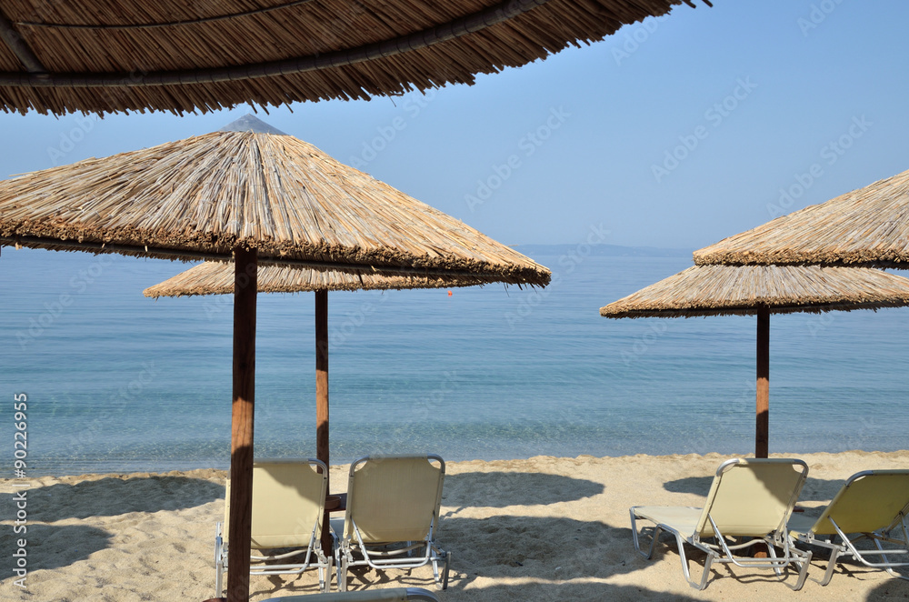 Beach straw parasols and pairs of chairs