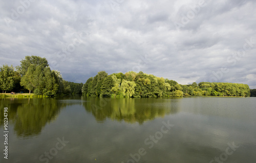 All shades of green lake island view with dramatic sky & water, people