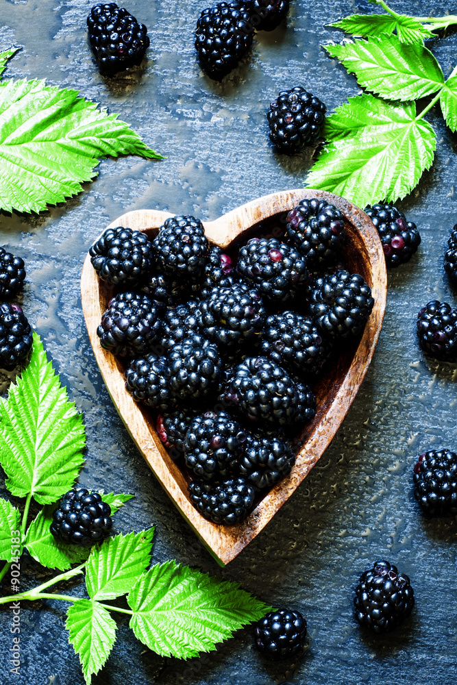 Fresh blackberries with green leaves in a bowl in the shape of a